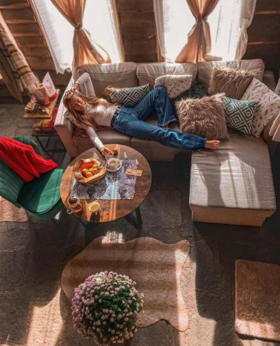 a woman laying on a couch in a living room at Панорама хаус Лещен и еко къщи Дървена и Землянка in Leshten