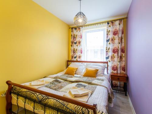 a bedroom with a bed with yellow walls and a window at Apartament Bursztyn in Kołobrzeg