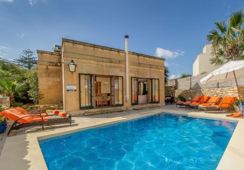 a swimming pool with orange chairs and a house at Casetta Menzja Semi Detached Bungalow in Sannat