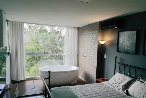 1 dormitorio con bañera y ventana grande en Loft Espaço Vila da Serra en Nova Lima