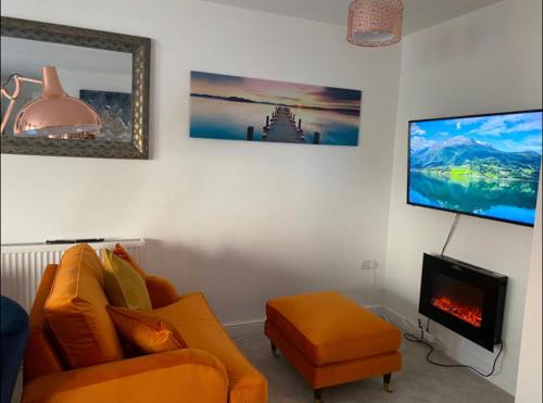 a living room with an orange couch and a tv at Luxury Modern 1Bed Sea View Apartment in Llandrillo-yn-Rhôs