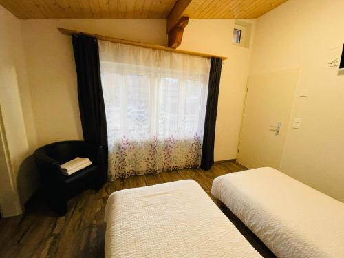 a bedroom with two beds and a window with a chair at Swiss Chalet Holidays Ringgenberg in Ringgenberg