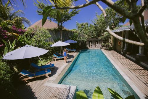 a woman standing next to a swimming pool with umbrellas at La Berceuse Resort and Villa Nusa Dua by Taritiya Collection in Nusa Dua