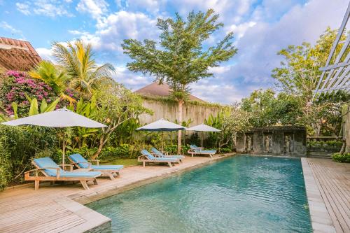 una piscina con sillas y sombrillas en un patio en La Berceuse Resort and Villa Nusa Dua by Taritiya Collection en Nusa Dua