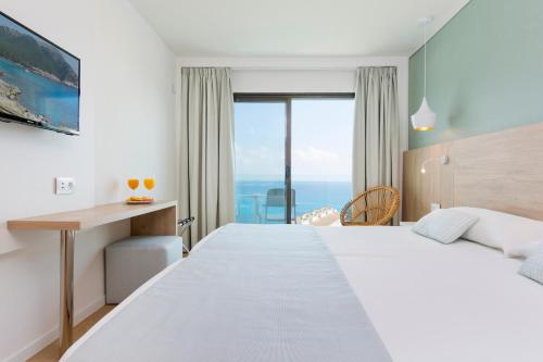 a bedroom with a large bed with a desk and a window at HSM Regana - Adults only in Cala Ratjada