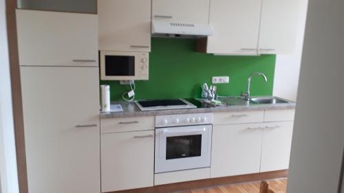 a kitchen with white cabinets and a green wall at City Appartment Orlitsch in Klagenfurt