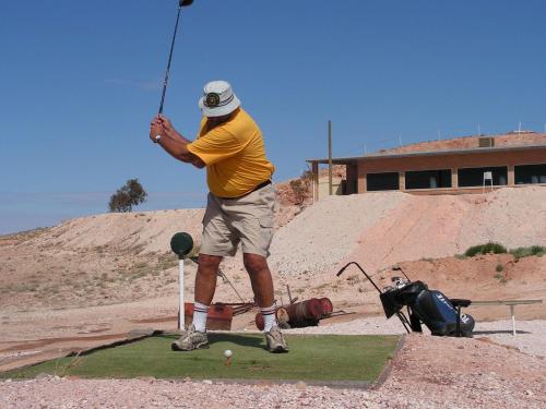 a man swinging a golf club on a putting green at Ali's Underground Studio in Coober Pedy