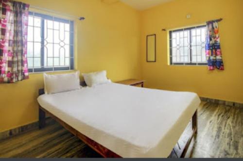Cama blanca grande en habitación amarilla con ventanas en Radhabai Hotel, en Arambol