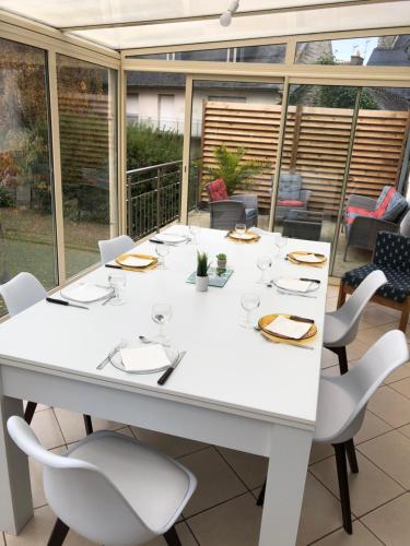 une table et des chaises blanches dans une chambre avec fenêtres dans l'établissement Gîte du Guildo, à Saint-Cast-le-Guildo