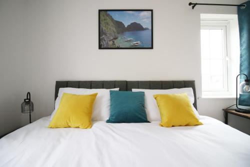 um quarto com uma cama branca com almofadas amarelas e azuis em DELFT - Spacious Home, High Speed Wi-Fi, Free Parking, Terrace em Swindon