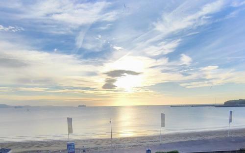 a view of a beach with the sun setting over the water at Sunrise View - Beachfront Apartment, Weymouth in Weymouth