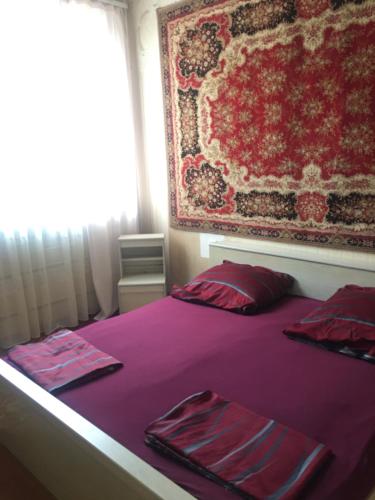 Cama morada con almohadas rojas y alfombra en Friendly B&B, en Gyumri