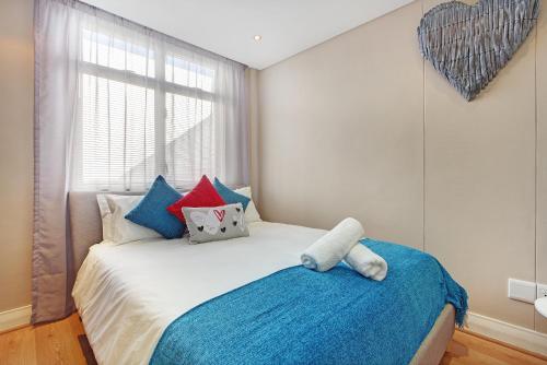 een slaapkamer met een bed met blauwe en rode kussens bij A Modern unit, self checkin, restaurants and shops below in Kaapstad