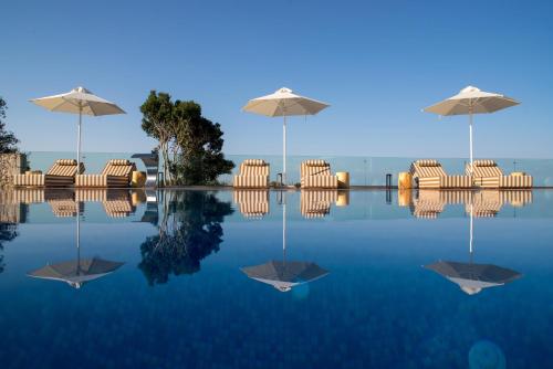 a pool with chairs and umbrellas in the water at Aliv stone suites & spa in Agios Nikolaos