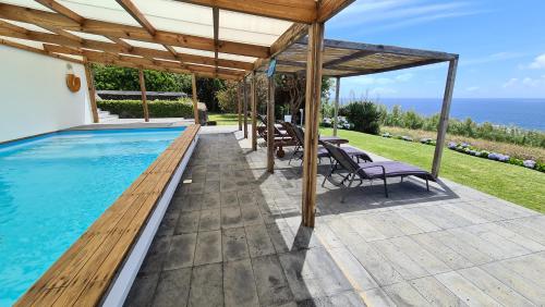 a swimming pool with a wooden pergola and chairs at Quinta da Meia Eira in Horta