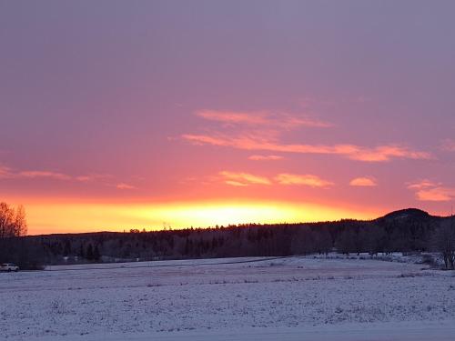 a sunset over a snowy field with the sun setting in the background at Danny in Mellansel