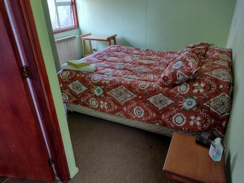 a small bedroom with a bed with a red comforter at Hostal El Toque de Pilar in Punta Arenas