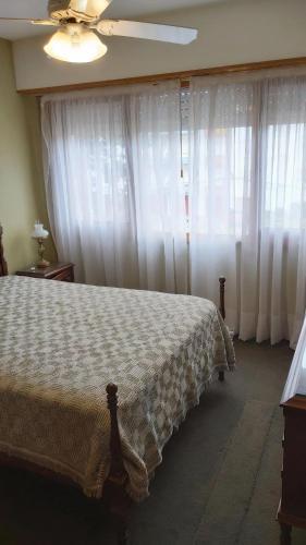 1 dormitorio con 1 cama con cortinas blancas y ventilador de techo en el Departamento Malevo en Villa Gesell