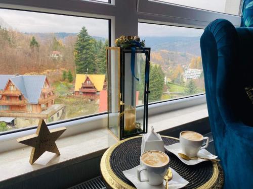 a table with two cups of coffee in front of a window at Apartament SPA 52 Resort Kozubnik blisko Szczyrk- 5D Apartamenty in Porąbka
