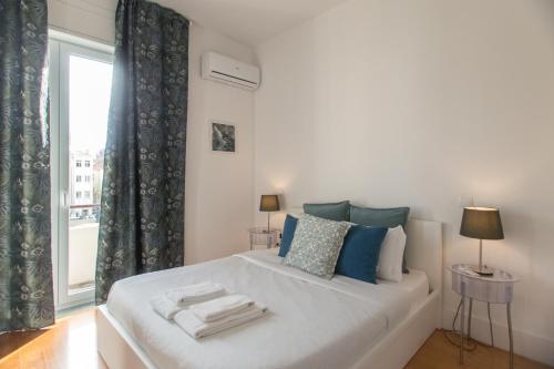 ein weißes Bett mit blauen Kissen und einem Fenster in der Unterkunft Pinpoint Porto Apartment by Porto City Hosts in Porto