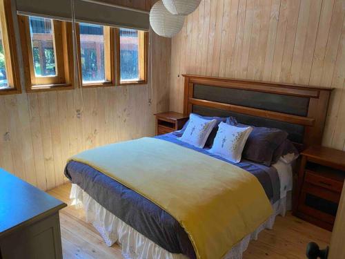 een slaapkamer met een groot bed met houten wanden en ramen bij Acogedora cabaña al borde del Río Claro in Pucón