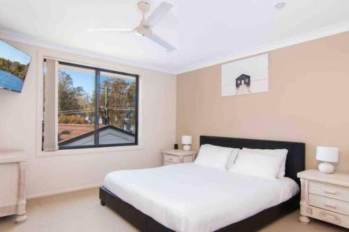 a white bedroom with a bed and a window at 4 Bedroom modern house opposite Wallis Lake in Forster