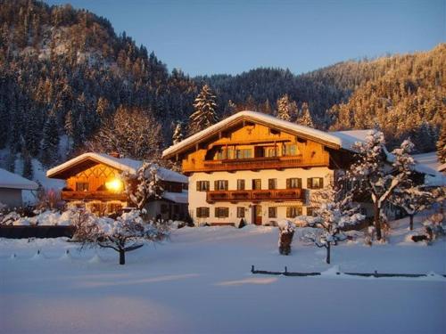 a large building in the snow with trees and mountains at Stoibhof Familie Klauser in Reit im Winkl
