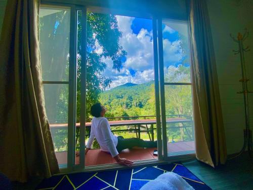 una persona sentada en el alféizar de una ventana mirando a las montañas en บ้านชายดอย Glamping ดอยแม่แจ๋ม cheason ,Muangpan, Lampang en Ban Mai