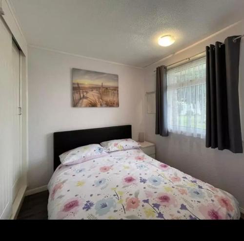 a bedroom with a bed with a floral comforter and a window at Chalet hemsby in Great Yarmouth