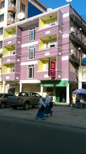dos personas caminando frente a un edificio rosa en Kibodya Hotel Nkrumah en Dar es Salaam