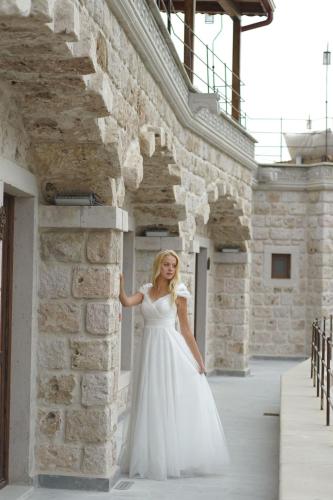 a woman in a white dress leaning against a brick wall at Göreme Cave Lodge in Goreme