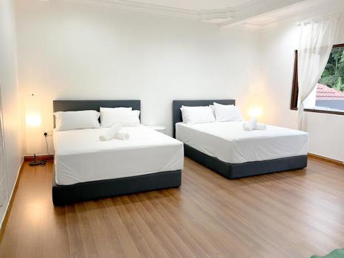 two beds in a room with white walls and wood floors at Mas Homestay in Kuala Lumpur