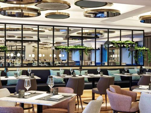 un restaurante con mesas, sillas y ventanas en Athens Capital Center Hotel - MGallery Collection en Athens