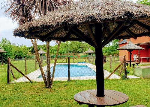 ein großer Strohschirm im Gras neben einem Pool in der Unterkunft Cabañas La Viña in Chascomús