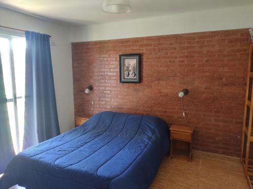 een slaapkamer met een blauw bed tegen een bakstenen muur bij Cabañas Olla Vieja in Santa Rosa de Calamuchita