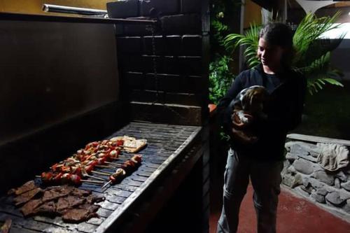 Un uomo che tiene un cane in piedi accanto a un grill di Villa Hospedaje Chanchan Cultural Lodge a Trujillo