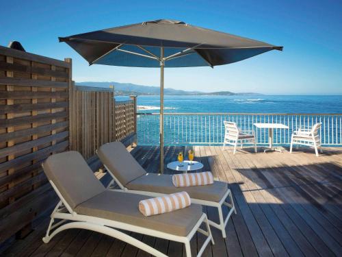 a patio with two chairs and an umbrella on a deck at Sofitel Golfe d'Ajaccio Thalassa Sea & Spa in Ajaccio