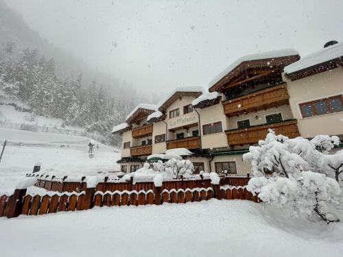 a building covered in snow with a fence and trees at Hotel La Maison Wellness & Spa in Alleghe