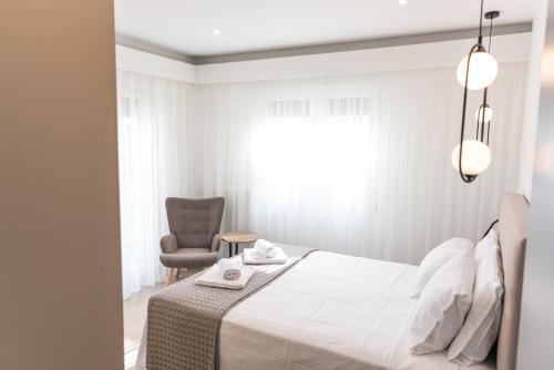 a white bedroom with a bed and a chair at Amelia Luxury Living in Volos