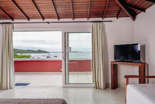 uma sala de estar com televisão e vista para o oceano em Mata Hari Apartamentos em Búzios