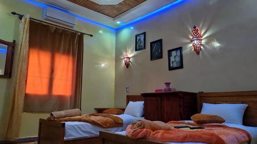 two beds in a bedroom with blue lights on the wall at Dar Calme Chez El Bouhali in Skoura