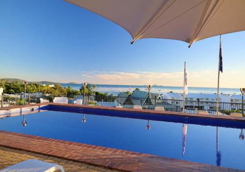 a swimming pool with an umbrella and the ocean in the background at Whitsunday Terraces Resort in Airlie Beach