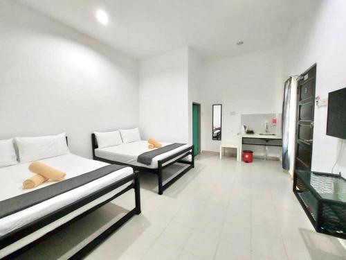 Cette chambre blanche comprend deux lits et un bureau. dans l'établissement Belukar Lodges Private Homestay, à Pantai Cenang