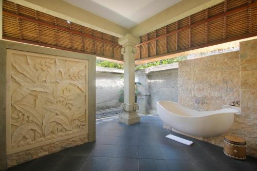 a bathroom with a bath tub and a wall at Santi Mandala Villa & Spa in Sukawati
