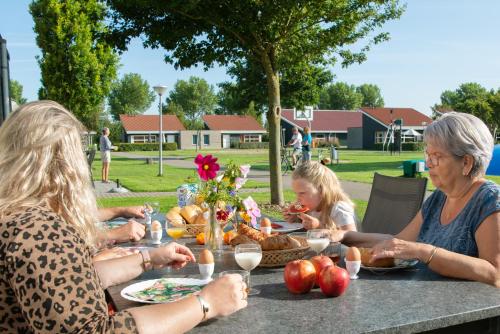 un grupo de personas sentadas en una mesa comiendo comida en Vakantiepark Broedershoek, en Koudekerke