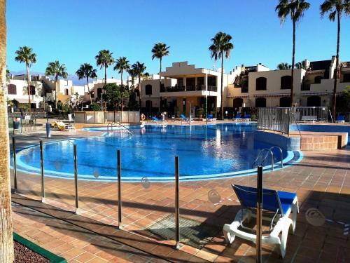 a swimming pool with a chair and palm trees at Apartment with large relax terrace and top equipment in Costa Del Silencio