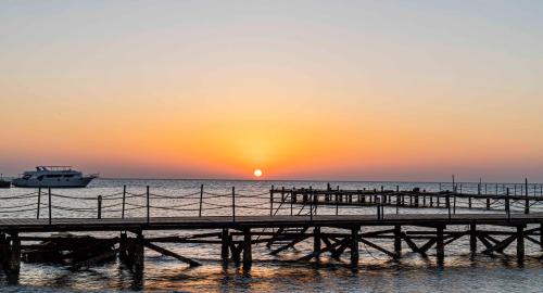 a pier with a boat in the ocean at sunset at Amarina Abu Soma Resort & Aquapark in Hurghada