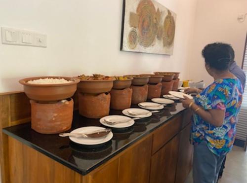 a woman standing in front of a counter with plates at Hummingbird Leisure Villa-Anuradhapura in Anuradhapura