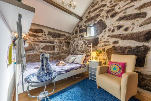 1 dormitorio con pared de piedra, cama y silla en Pequena Casa rústica com piscina, en Penafiel