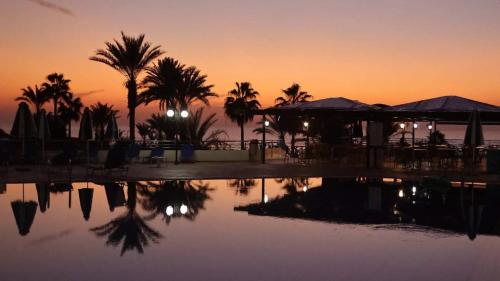 a pool of water with palm trees and a sunset at Helios Bay Hotel and Suites in Paphos